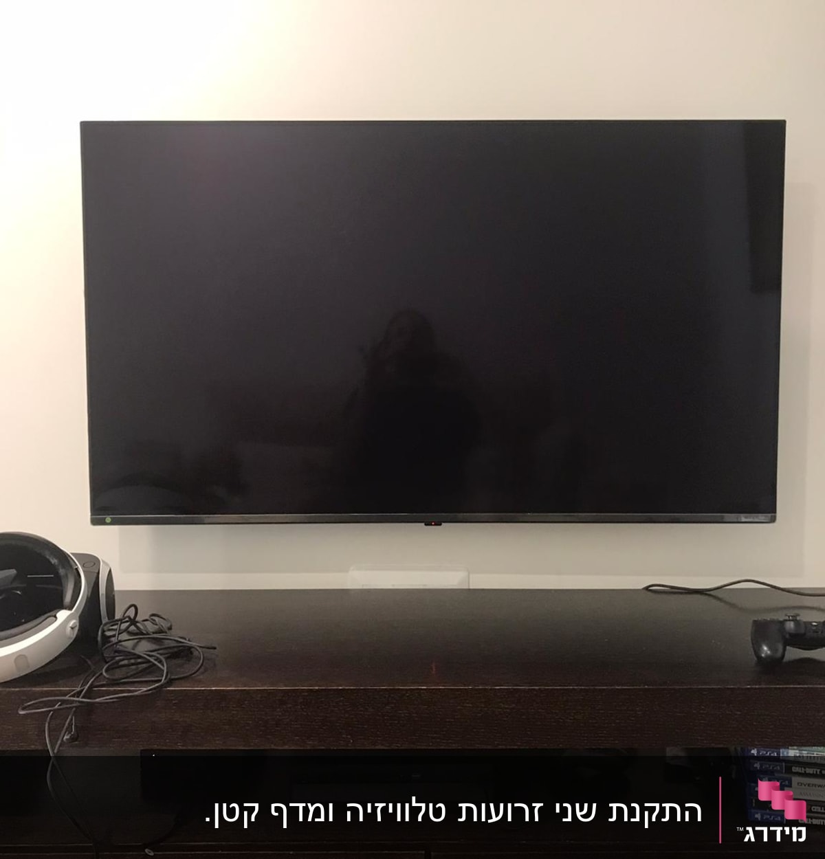 טלוויזיה תלויה על הקיר עם אוזניות ושלט על מדף